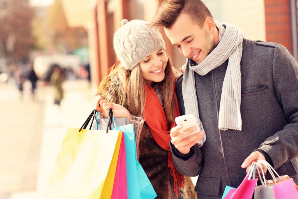 Happy couple shopping in the city with smartphone